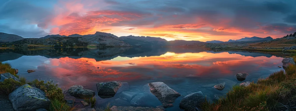 a majestic landscape unfolds at dawn, where vibrant hues of orange and pink saturate the sky, casting a warm glow over a tranquil lake reflecting the surrounding rugged mountains.