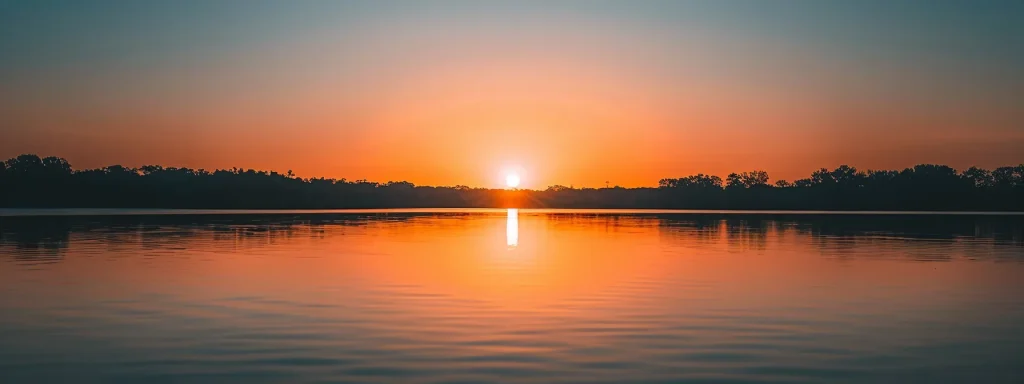 a majestic sunset casts vibrant hues of orange and pink across a tranquil lake, reflecting the stunning silhouette of distant mountains under a clear sky.