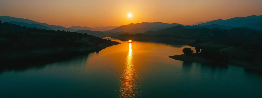 a mesmerizing sunset over a tranquil lake, with vibrant hues of orange and pink reflecting on the shimmering water, surrounded by silhouetted mountains under a clear sky.