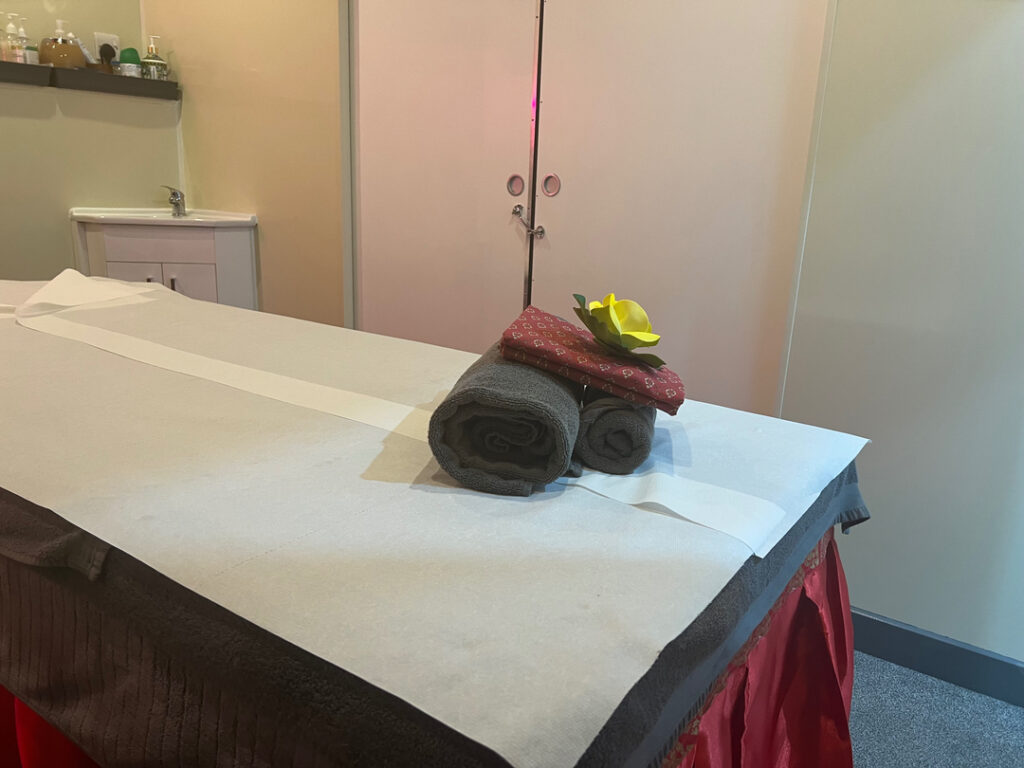 A serene massage room featuring a neatly prepared massage table with a rolled towel, decorative fabric, and a yellow flower, creating an inviting atmosphere for relaxation and therapy.