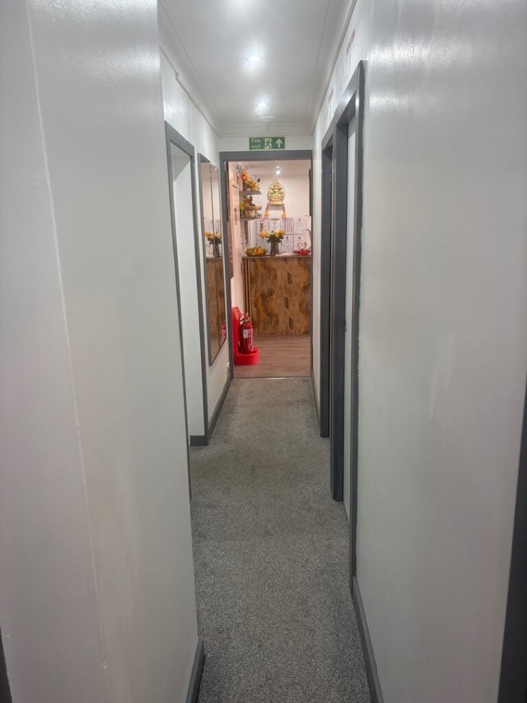 A well-lit hallway in a massage spa leading to a reception area adorned with floral arrangements and decorative accents, creating a welcoming atmosphere in a massage therapy center in Woolmer Green.