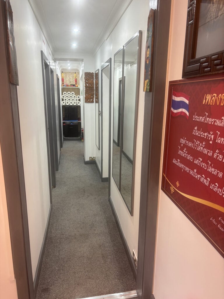 A warmly lit hallway inside a massage spa, featuring decorative elements and a neatly arranged shelf with rolled towels, reflecting a serene and inviting atmosphere.